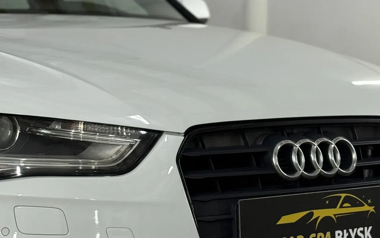 Przód białego Audi A4 po myciu, w miejscu tablicy plakietka Car-Spa Błysk